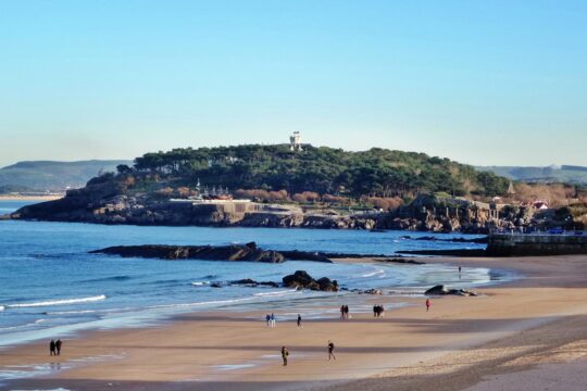 Familia disfrutando de un día soleado en la Playa de San José, con sombrillas y niños jugando en la orilla.